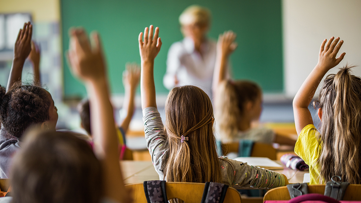Elementary students raising their hands in class