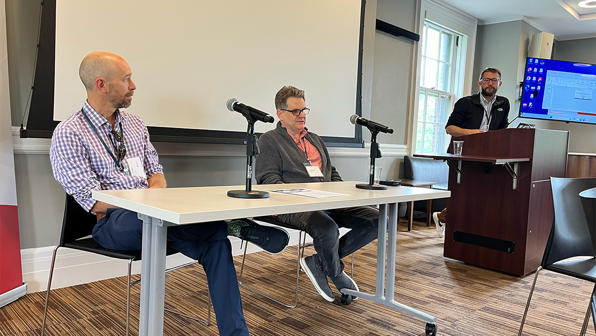 An image from a workshop eaturing two speakers at a table, and one person standing up. 