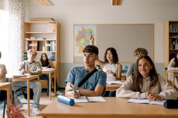 Girls and boys learning while sitting at desk in classroom 